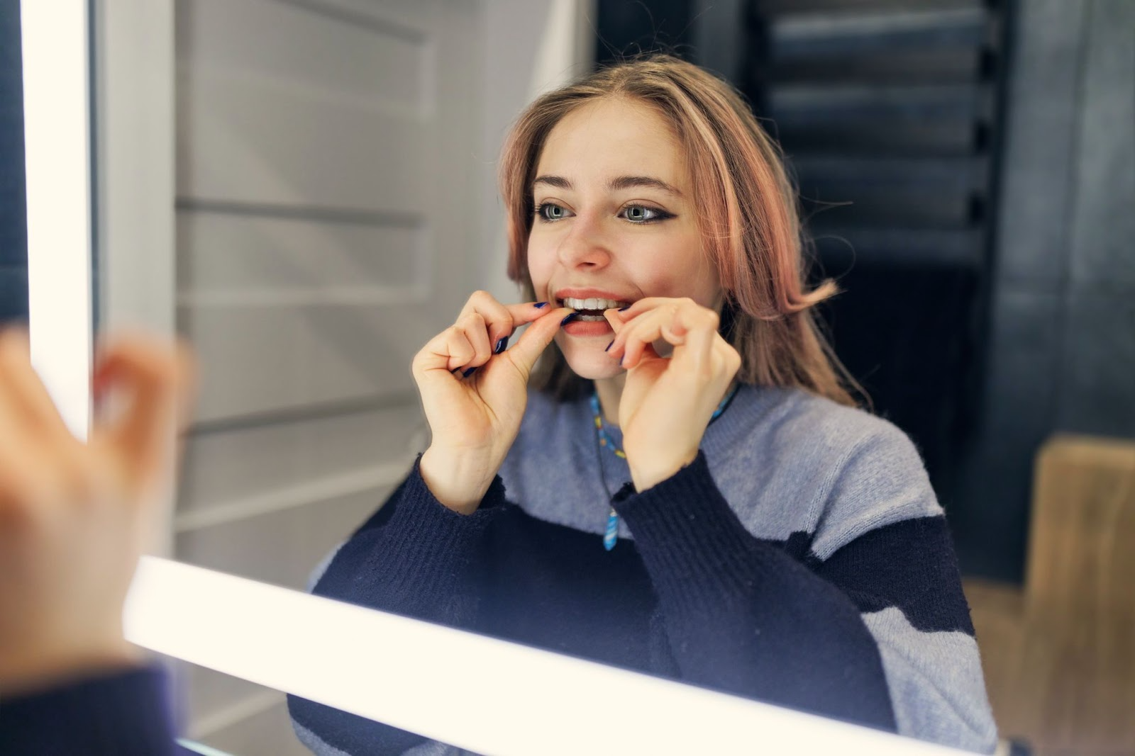 Woman applying clear aligners while looking in a mirror, demonstrating personal orthodontic care and the clear aligner treatment process.