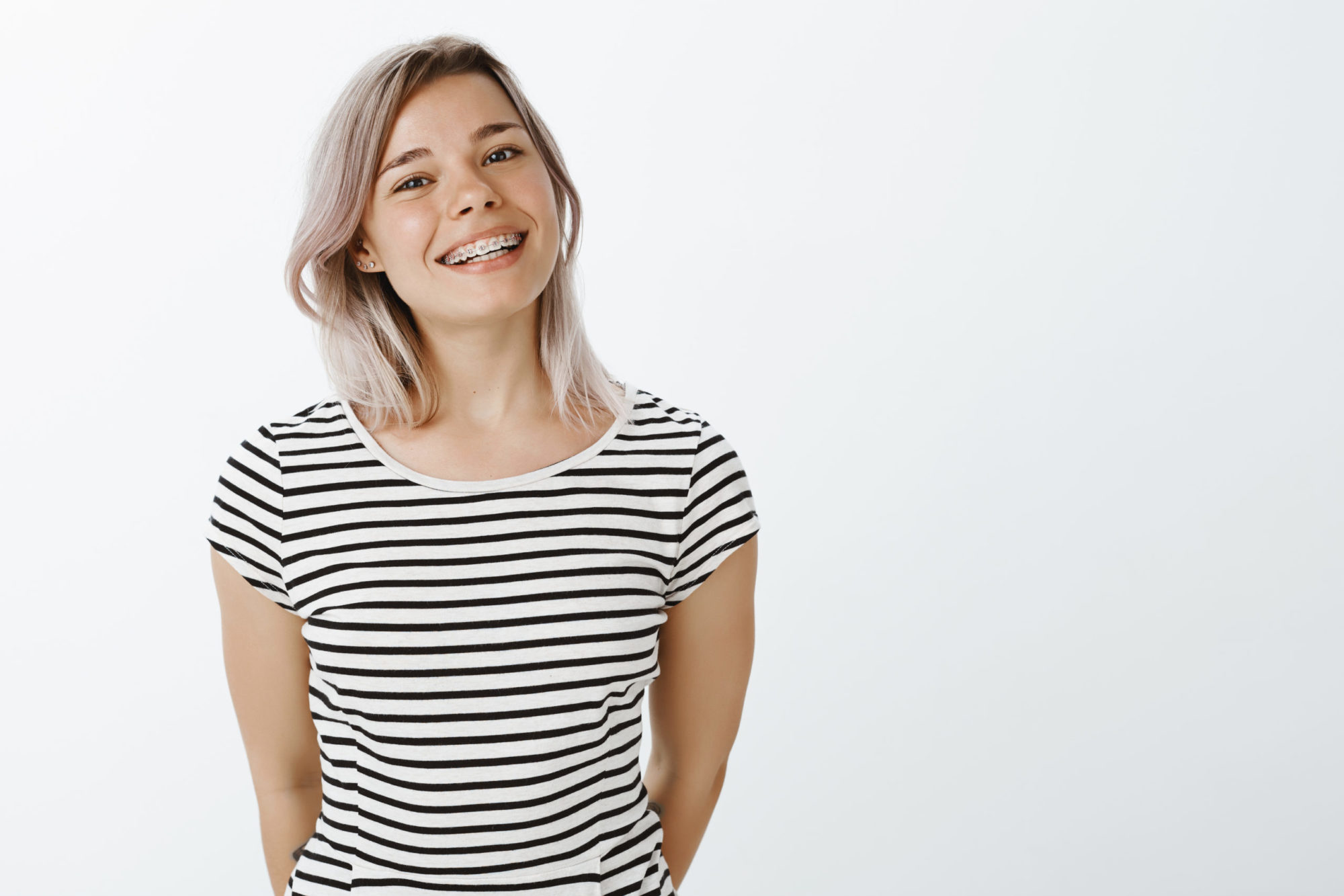Smiling young woman with braces wearing a striped shirt, representing orthodontic care at Complete Dental Studio in Boerne, TX.